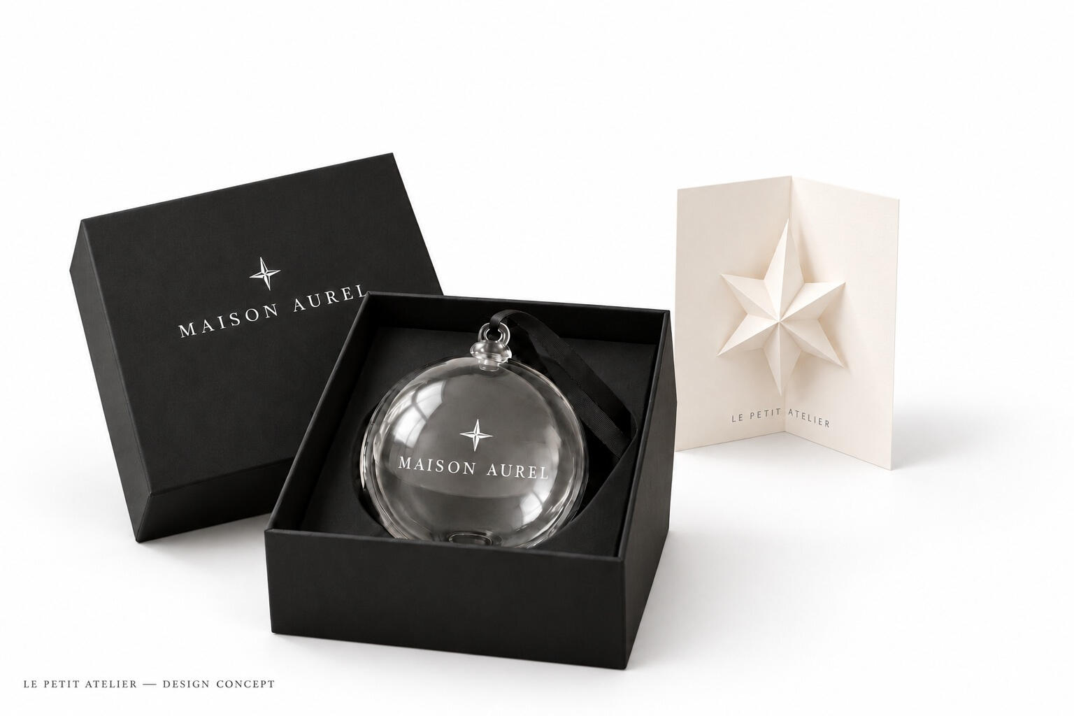 Saisonales Konzept MAISON AUREL: Weihnachtskugel aus Glas mit weißem Druck, schwarze Geschenkbox und plastische Stern-Grußkarte vor weißem Hintergrund.